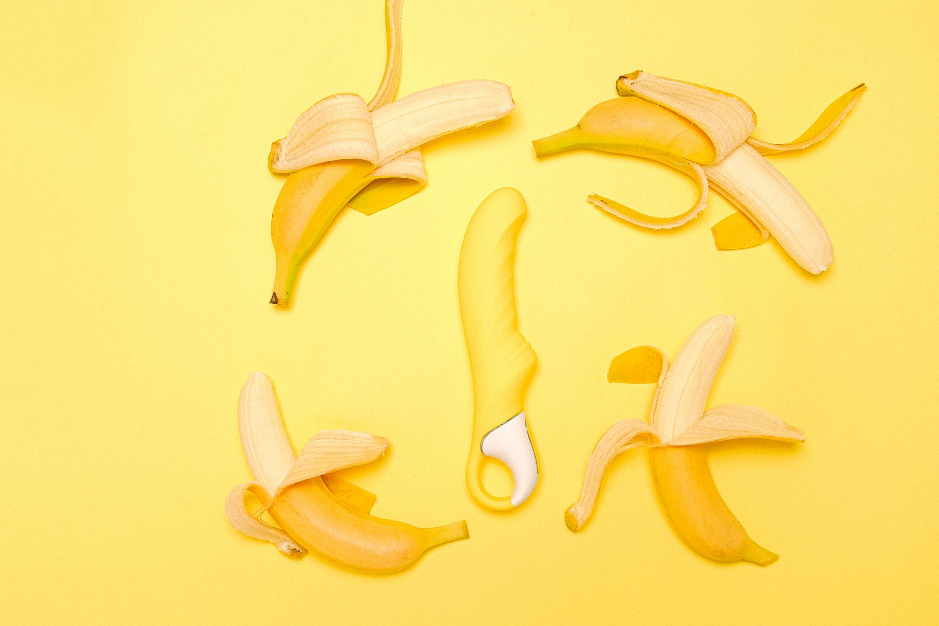 Yellow lemon-shaped vibrator surrounded by fresh fruit on bright background